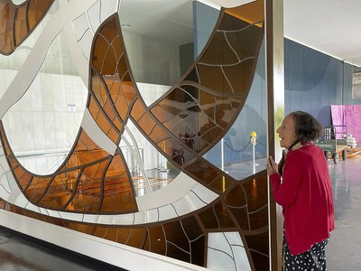 Artista plástica Marianne Peretti visita suas obras no Congresso Nacional.  Única mulher na equipe de Oscar Niemeyer na construção da nova capital, a artista Marianne Peretti deixou sua marca pelo Congresso Nacional. No Salão Branco não há como não perceber o painel Alumbramento, doado em 1978 ao Senado Federal. No Salão Verde é exibida a obra Araguaia. As cores e formas de seus vitrais estão também no Salão Nobre, onde pode ser apreciado o vitral Phasifae. No 10º andar do Anexo IV da Câmara dos Deputados, suas mãos foram as responsáveis pelos vitrais da capela. Também na Casa Legislativa, outra obra de destaque: um painel com sobreposição de camadas de vidro, de 1977.  Na foto, Marianne Peretti posa para fotografia ao lado do painel "Pasiphae", 1977.  O painel é confeccionado em vidro artesanal e cristal branco fosco e marrom. O título remete à mitologia grega, pois Pasiphae é o nome da filha do deus-sol Hélio, esposa do Rei Minos e mãe de Minotauro. A peça foi restaurada em 2010, em comemoração aos 50 anos da Câmara dos Deputados em Brasília.  Foto: Walesca Borges/Senado Federal